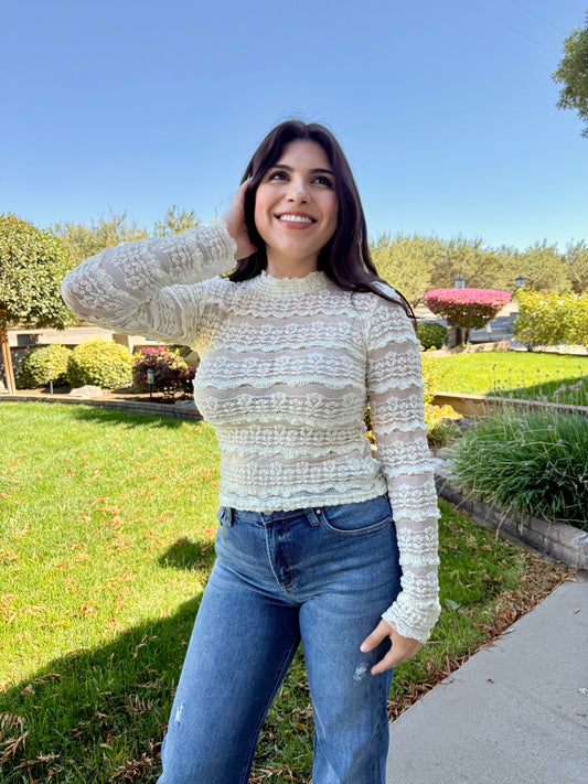 Woman wearing a light sweater and jeans standing outdoors on a sunny day.