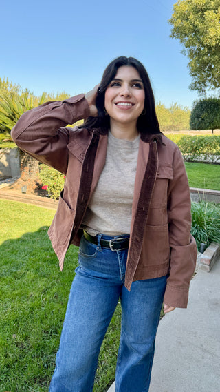 A woman wearing a beige sweater with a brown barn jacket outdoors.
