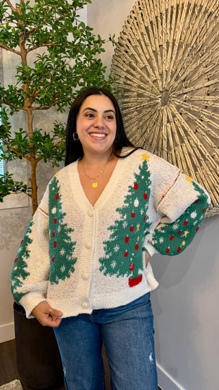 Woman wearing a festive sweater with Christmas tree patterns indoors.