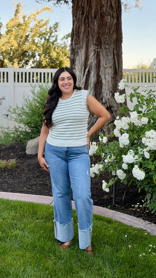 Woman wearing a white and sage striped sleeveless crocheted knit top with cuffed jeans. 