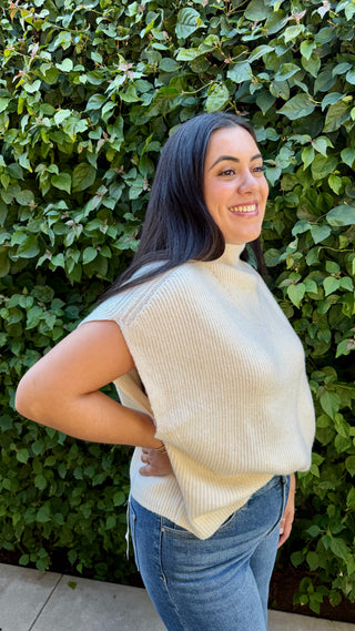 Woman wearing a ivory knitted sweater vest and blue jeans.