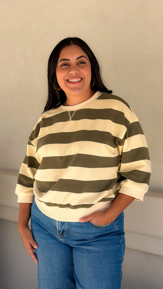 Woman wearing an olive and cream bold stripe notched V-neck top with blue jeans
