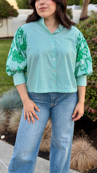 Woman wearing a green shirt with green floral sleeves.
