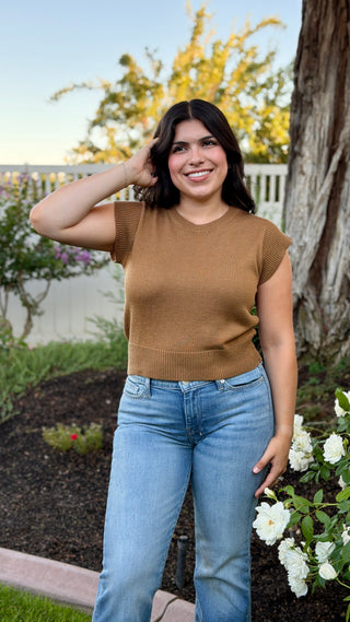 Woman wearing a camel cap sleeve knit sweater top with a ribbed hem.