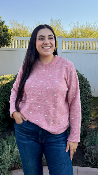 A woman wearing a pink polka dot sweater with blue jeans.