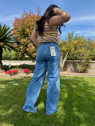 A woman wearing high waisted jeans that are a medium wash with a raw hem and are a wide leg style. 