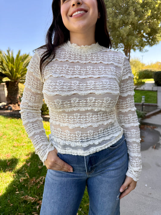 Woman wearing a light sweater and jeans standing outdoors on a sunny 