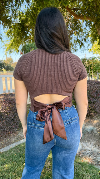 Woman wearing a brown top knitted top with a satin tie on the back and blue jeans.