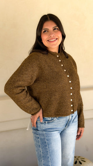 Model in olive brown ribbed knit cardigan sweater worn as a top with light blue jeans, angled front view