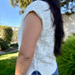 Person wearing a white sleeveless knitted top outdoors with greenery in the background