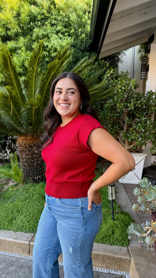 Woman wearing a cherry red cap sleeve knit sweater top with a ribbed hem.