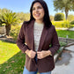 Woman wearing a brown blazer outdoors with greenery in the background