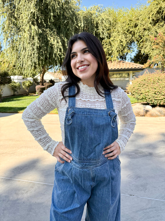 Woman wearing blue denim overalls with a white lace long sleeve 
