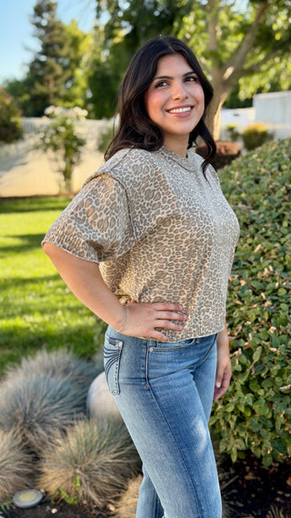 Woman wearing a neutral leopard print ribbed knit short sleeve top with a crew neckline, rolled sleeves, and a slightly cropped fit paired with medium wash jeans.