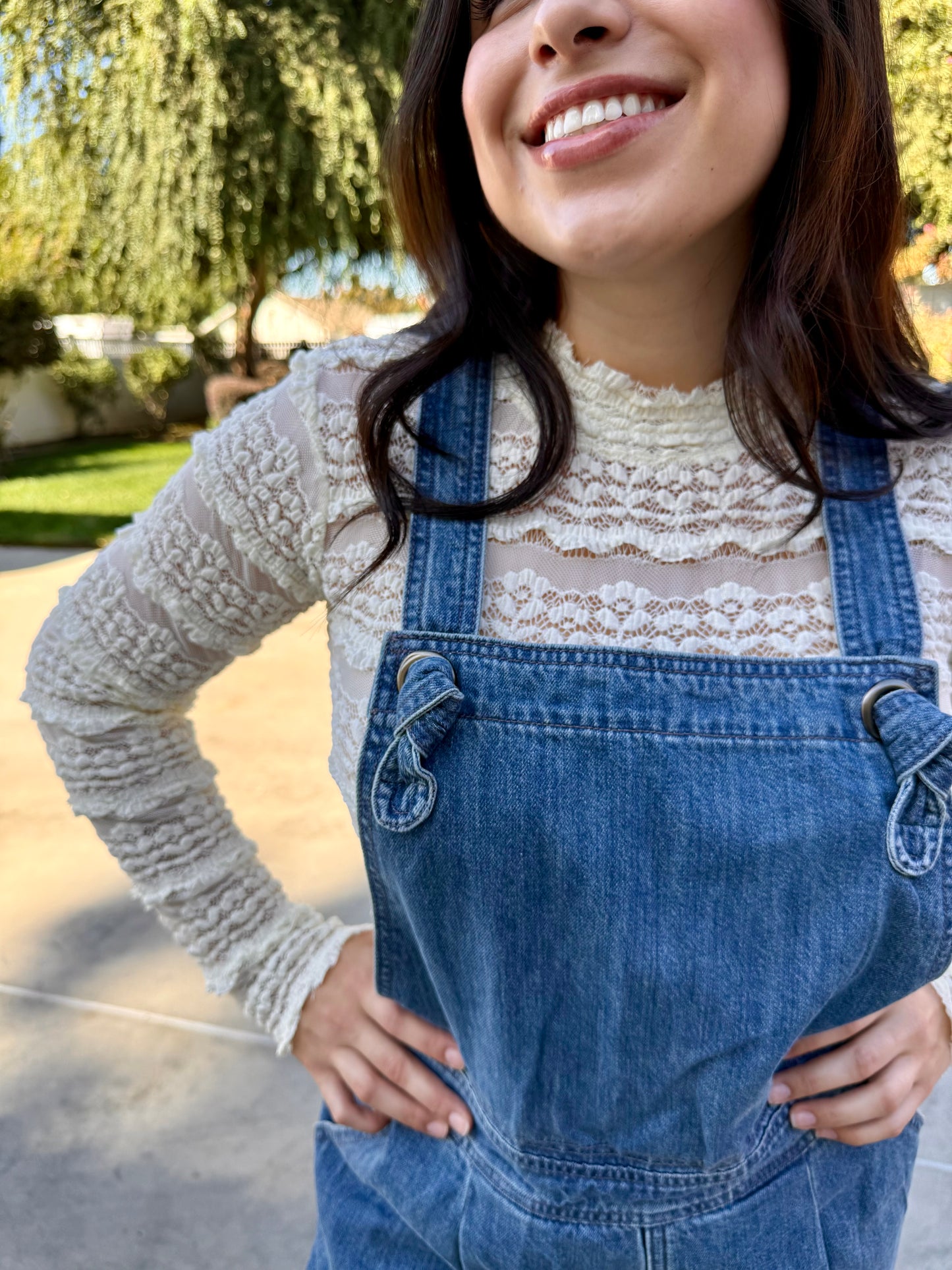 Woman wearing blue denim overalls with a white lace long sleeve outdoors
