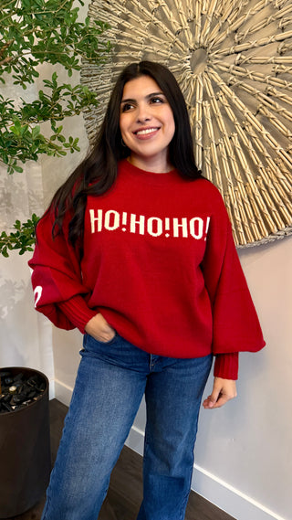Person wearing a red sweater with 'HO! HO! HO!' text, standing indoors.