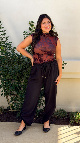 Model wearing black wide leg drawstring pants with ruched ankle ties and a burgundy sleeveless top, full-length front view