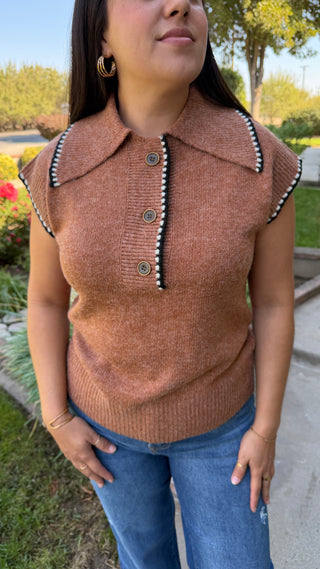 Woman wearing a brown sleeveless sweater with decorative black and white trim.