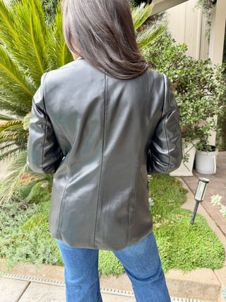 Woman wearing a black leather jacket and patterned top outdoors and blue jeans.