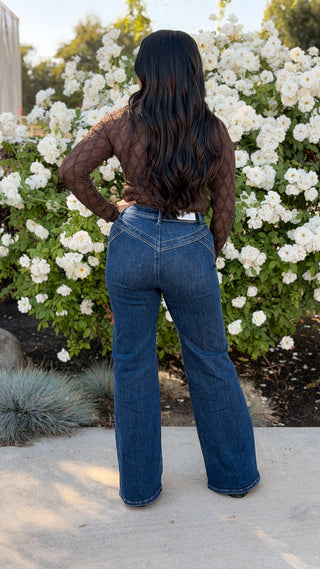 Woman wearing Risen high rise wide leg jeans in dark wash, full-length back view with brown lace top