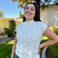 Woman wearing a light blue knitted top outdoors with trees and a fence in the background