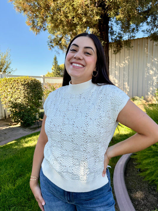 Woman wearing a light blue knitted top outdoors with trees and a fence in the background