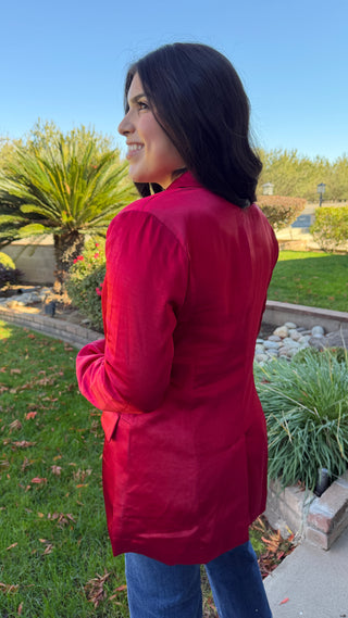 Woman wearing a long sleeve red satin blazer and blue jeans.