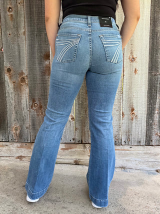 woman wearing blue jeans standing against a wooden fence.