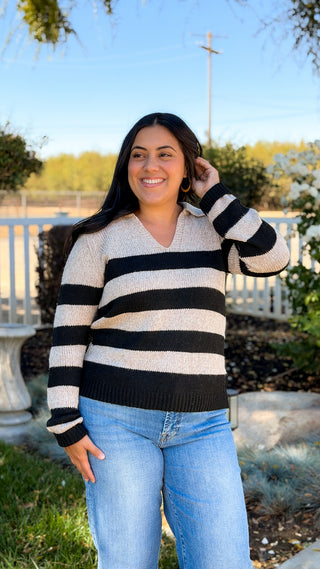 Women's black and cream striped sweater styled with blue jeans outdoors, full-length front view