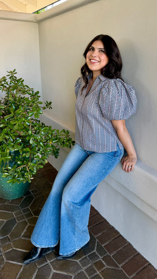 A woman wearing a black plaid blouse with jeans.