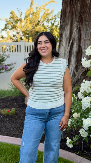 Woman wearing a white and sage striped sleeveless crocheted knit top.