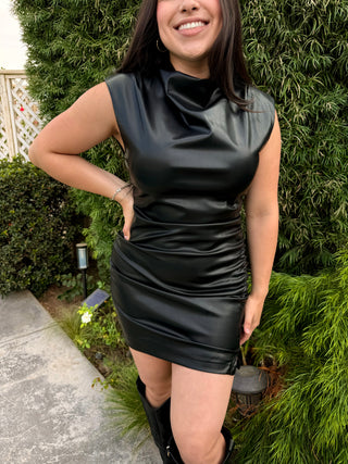 A woman wearing a sleeveless, high-neck, ruffled faux leather dress with a large zipper at the back. 