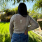 Person wearing a beige sweater and blue jeans standing in a garden