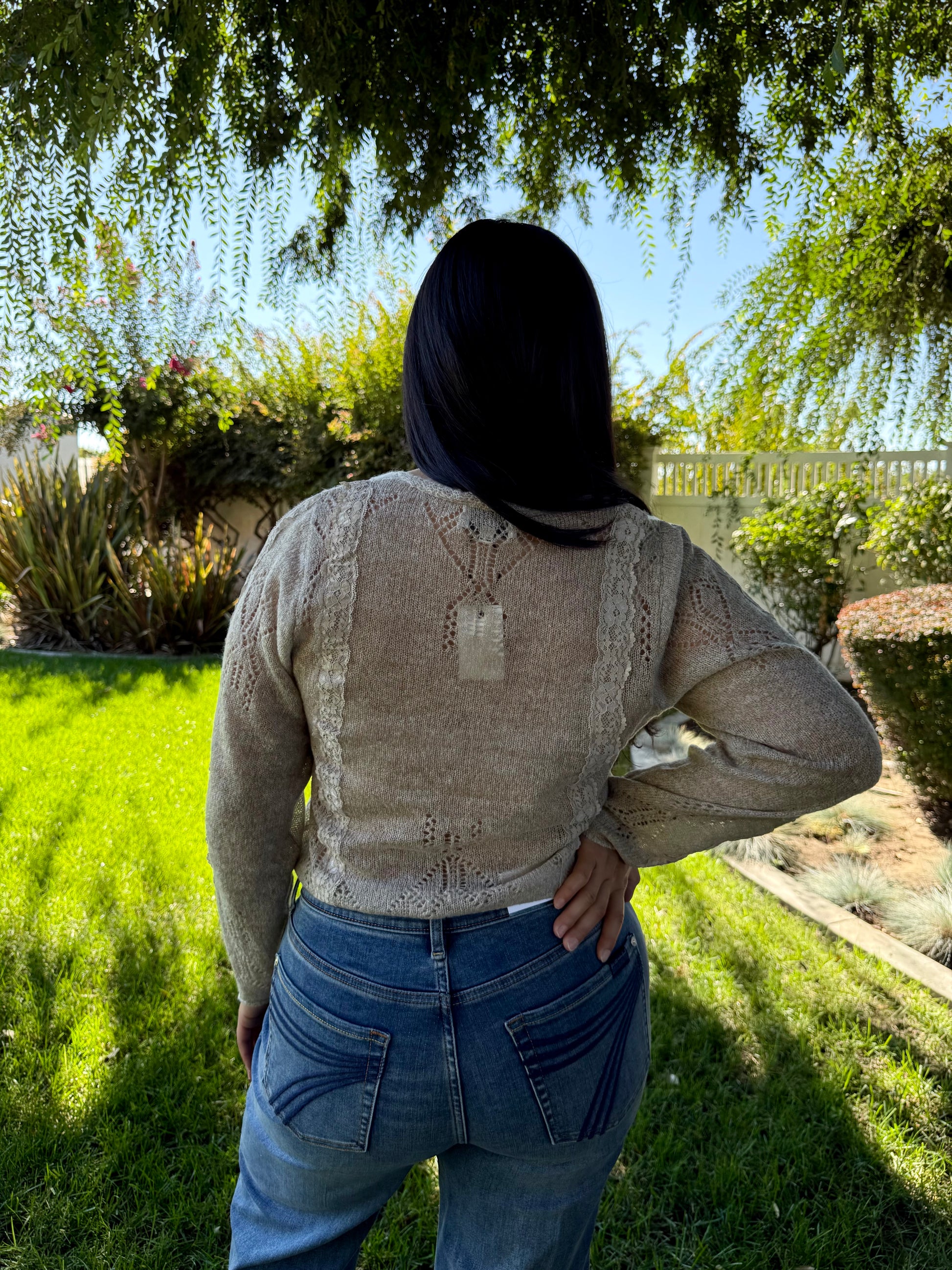 Person wearing a beige sweater and blue jeans standing in a garden
