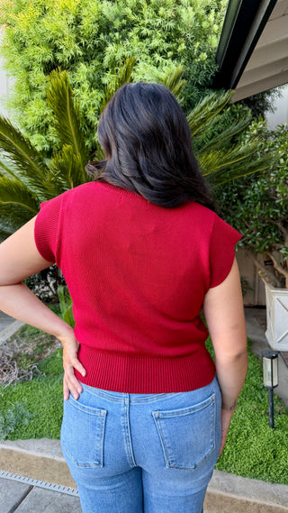Woman wearing a cherry red cap sleeve knit sweater top with a ribbed hem.