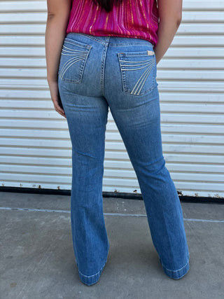 A woman wearing light-wash, mid-rise denim jeans showing the back pocket detail.