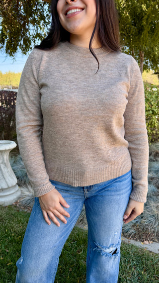 A woman wearing a long sleeve beige sweater with blue jeans outdoors.
