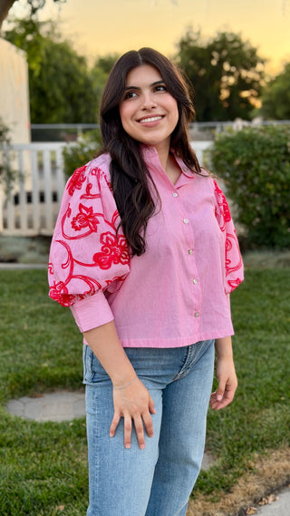 Woman wearing a red blouse with red floral embroidery and blue jeans.