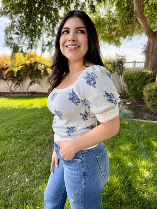 A woman wearing a short sleeve square neck top with a blue floral pattern while wearing blue jeans. 
