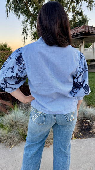 Woman wearing a button up in light blue shirt with patterned sleeves.