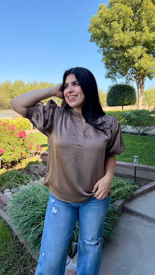 Woman wearing a brown blouse and blue jeans.
