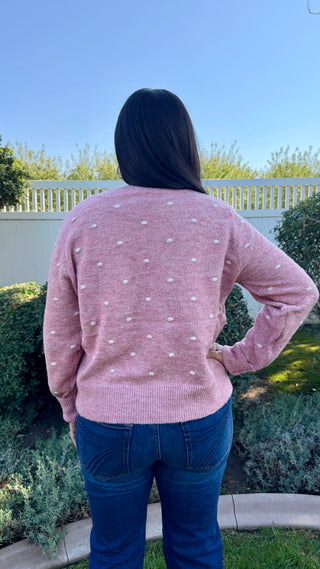 Person wearing a pink polka dot sweater and blue jeans standing outdoors.