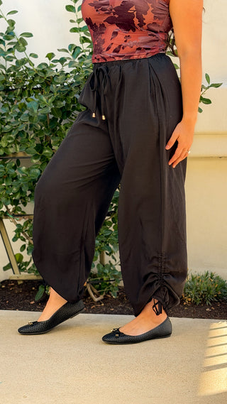 Side view of black lyocell-linen wide leg pants with ruched ankle ties gathered into a jogger-style fit, paired with black ballet flats