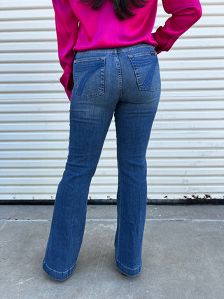 A woman wearing medium wash blue jeans with a blue 7 stitching on the back pocket. 