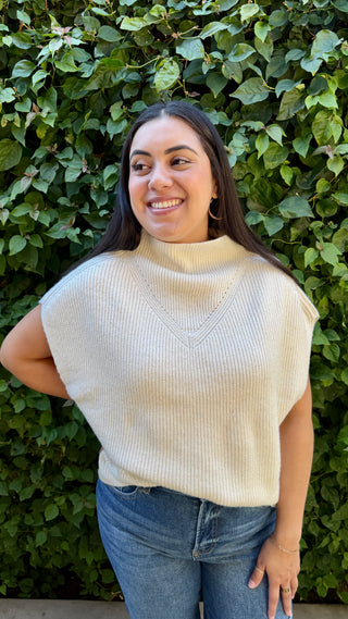 Woman wearing a ivory knitted sweater vest and blue jeans.
