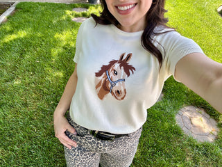 Woman wearing a cream short-sleeve sweater with a horse graphic, paired with leopard-print pants.