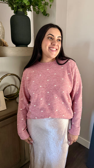 Woman wearing a pink sweater with white polka dots indoors.