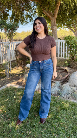 Woman wearing a brown top knitted top with a satin tie on the back and blue jeans.
