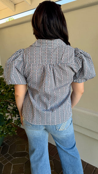 A woman wearing a black plaid blouse with jeans.