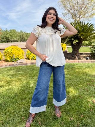A woman wearing high rise wide leg jeans with a big cuff on the bottom in a dark wash. 